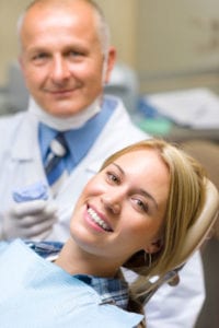 a woman smiling from the dentist chair with her dentist smiling beside her