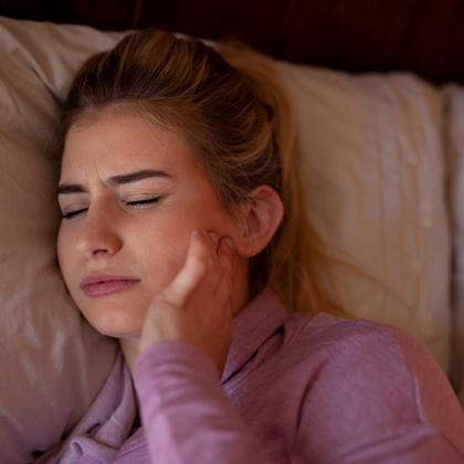 Young woman lying on a pillow and holding the side of her face portraying a TMJ flare-up